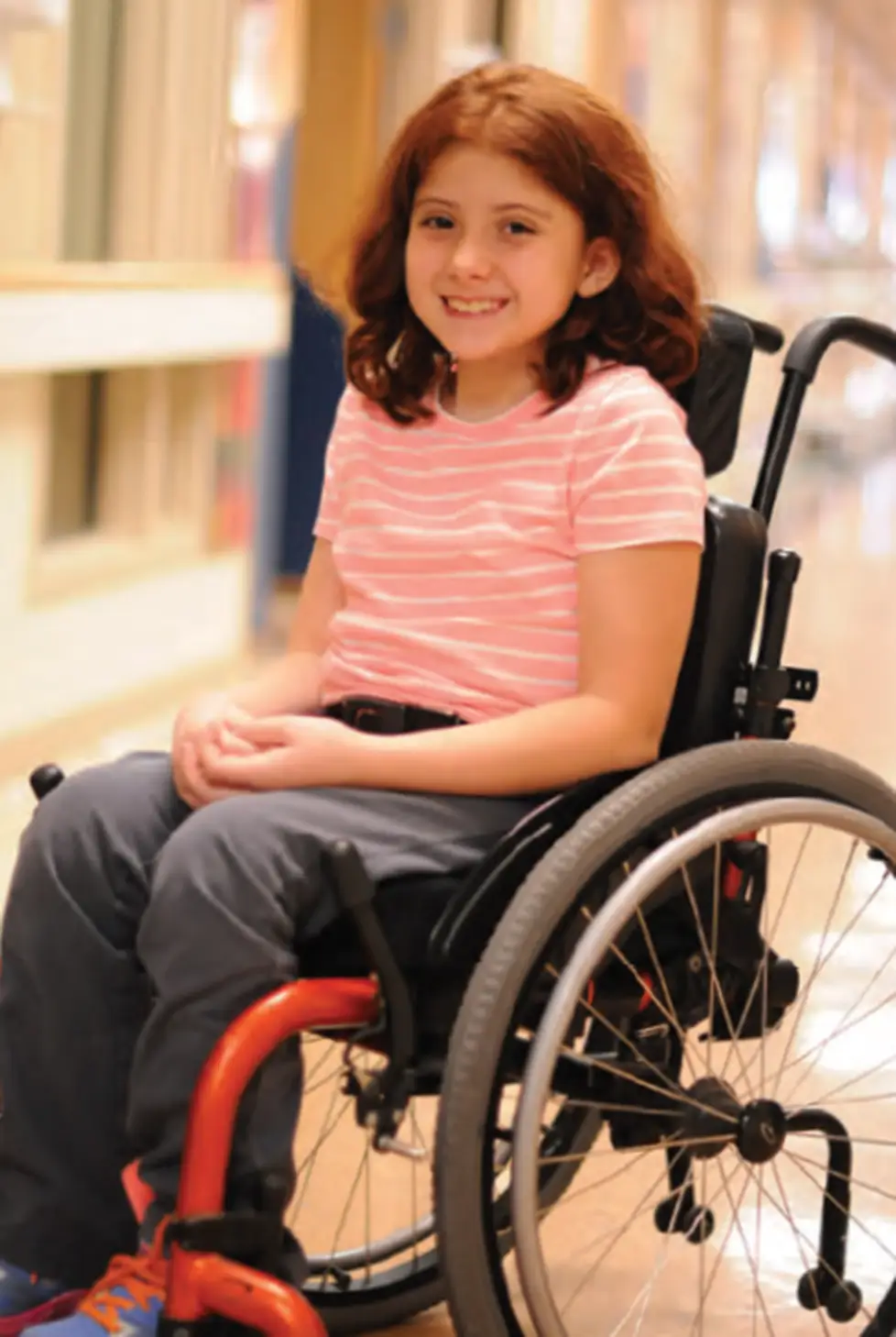 Smiling young girl sitting in a wheelchair indoors.